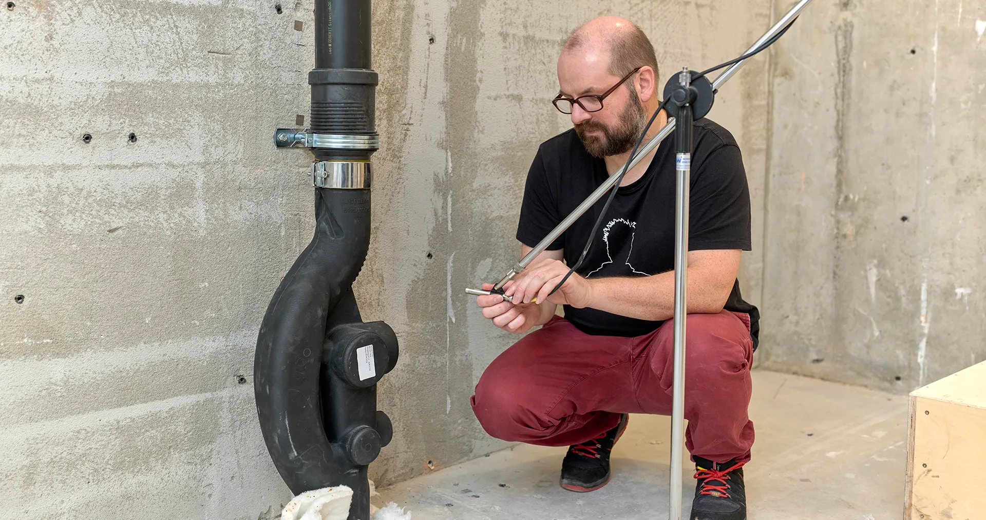 A man wearing glasses kneeling and preparing a measurement in the Technology and Acoustics Laboratory in Rapperswil-Jona (CH). (Photo)