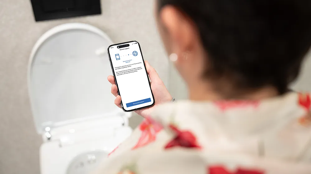 A woman is using the Geberit Home app, which allows users to grant customer service staff temporary access to their shower toilet. (Photo)