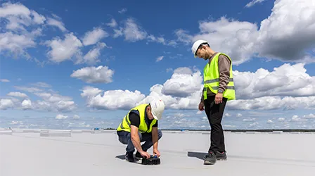 Installing of the roof drainage system Geberit Pluvia by two workers wearing yellow vests.&nbsp; (Photo)